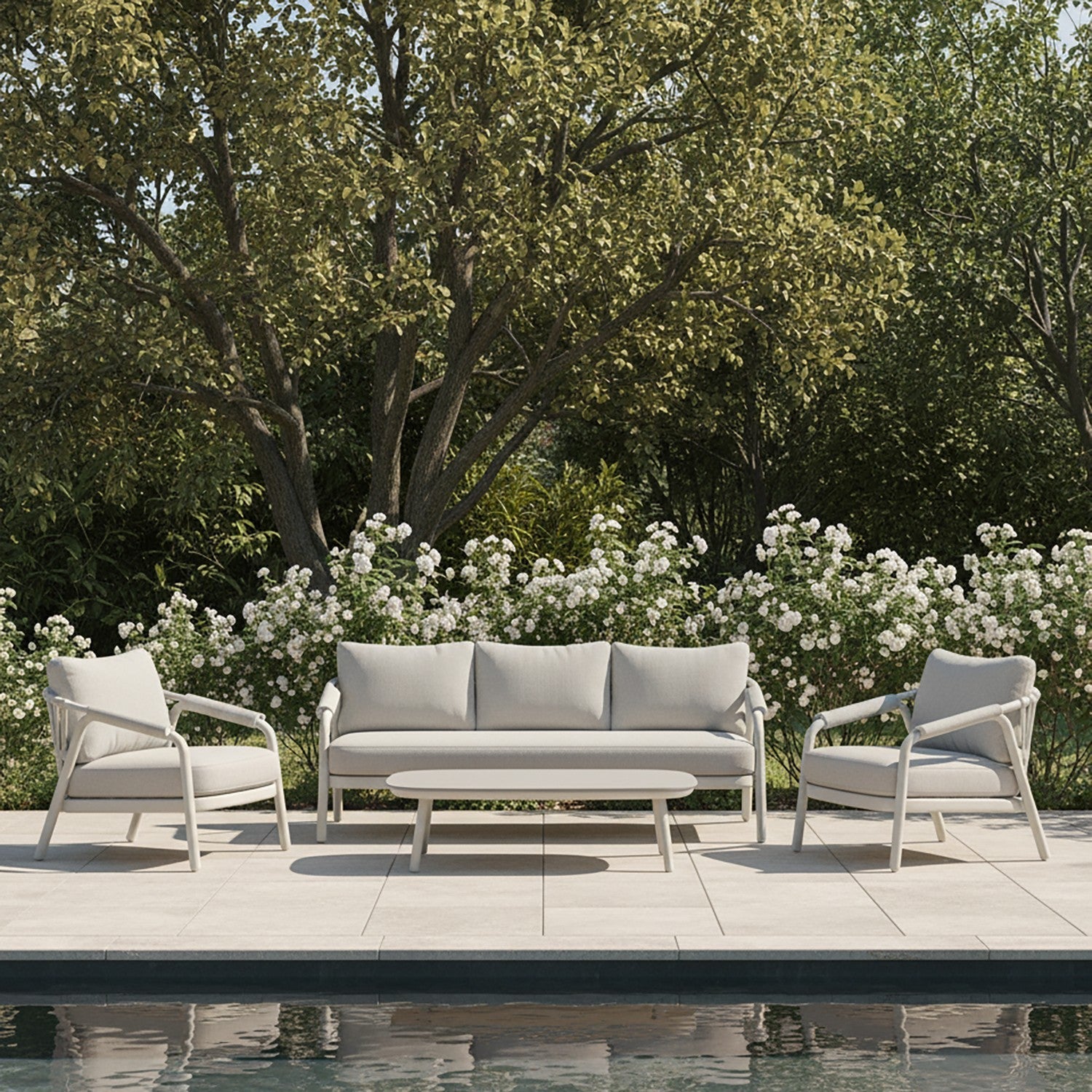 A modern grey outdoor lounge with 3 decorative pillows and an outdoor coffee table, set against a green wall. We see 2 pot plants & a cup of tea on the coffee table.
