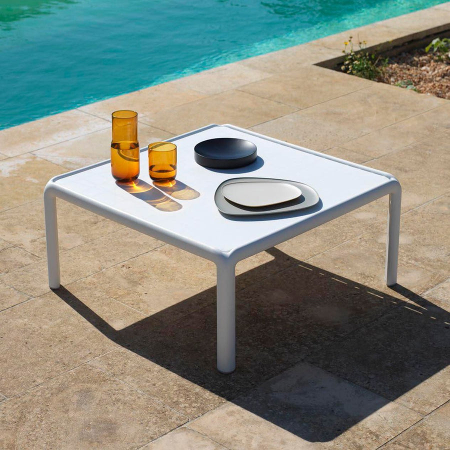 White outdoor coffee table by a pool, creating a serene outdoor setting.