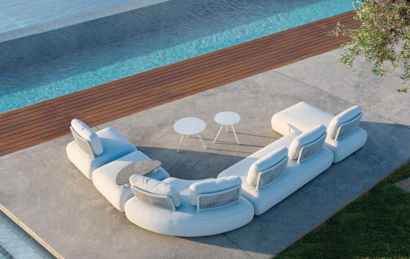 Aluminium outdoor furniture, Iowa coffee table in light grey, part of outdoor dining furniture set next to a white couch on a cement floor by a pool.