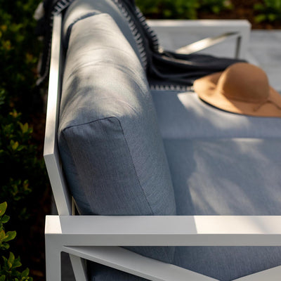 Aluminium outdoor furniture from Linear Lounge collection, featuring a white framed lounge with light grey cushions, a brown hat on top, and plants in the background.