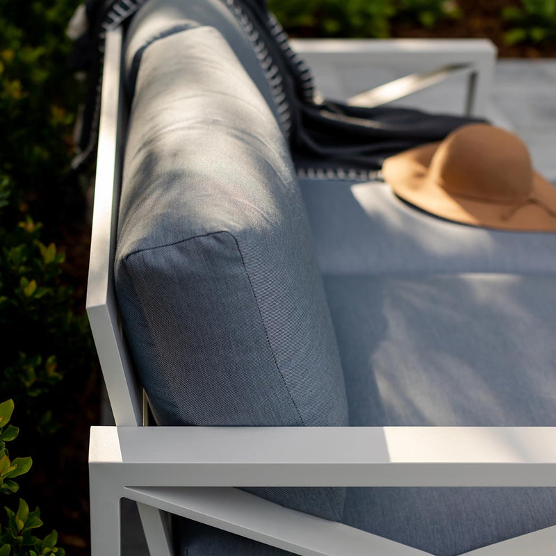 Aluminium outdoor furniture from Linear Lounge collection, featuring a white framed lounge with light grey cushions, a brown hat on top, and plants in the background.