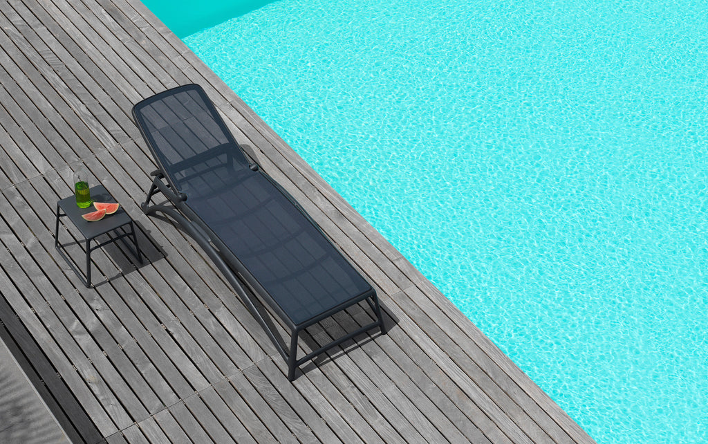 Nardi Atlantico sunlounger and Nardi Pop Outdoor Resin Coffee Table on a poolside deck. On the table is a bottle and slices of watermelon, creating a leisurely and comfortable atmosphere for enjoying a sunny day by the pool.