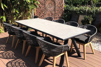 A wooden deck featuring a 10 seater outdoor table surrounded by chairs, creating an inviting outdoor dining space.