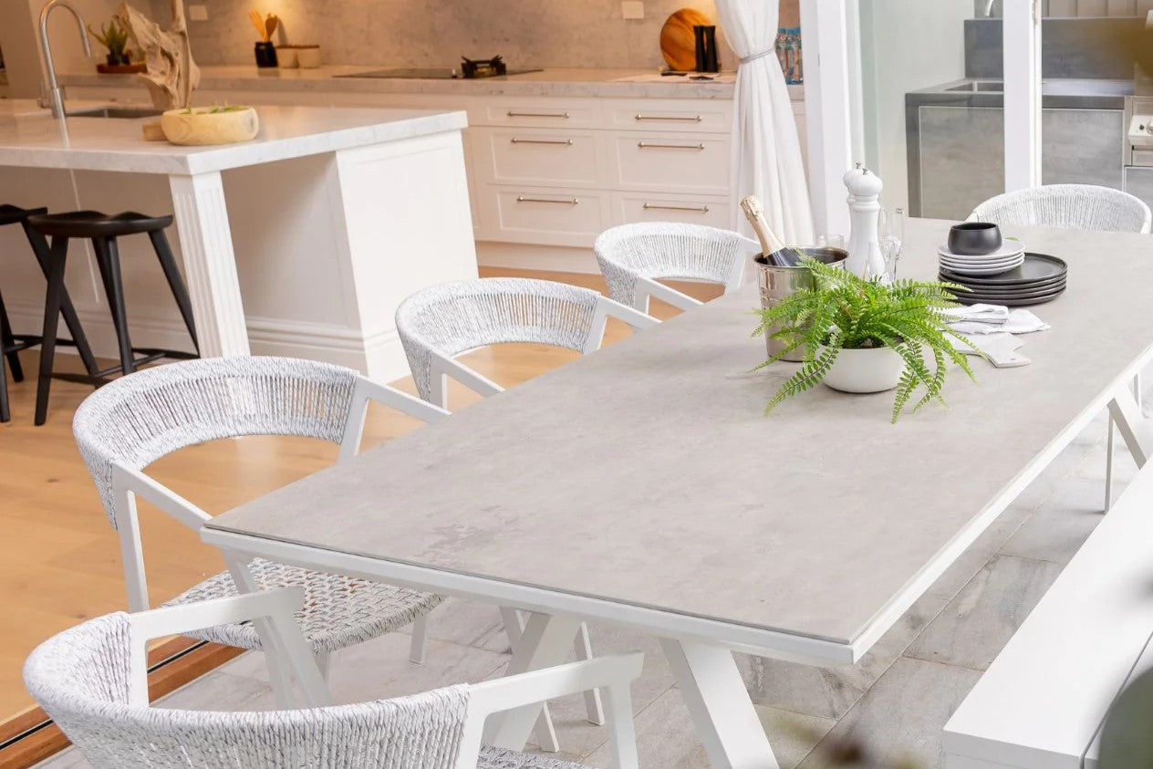 A sleek white ceramic outdoor table surrounded by matching chairs, elegantly set in a contemporary outdoor dining area.