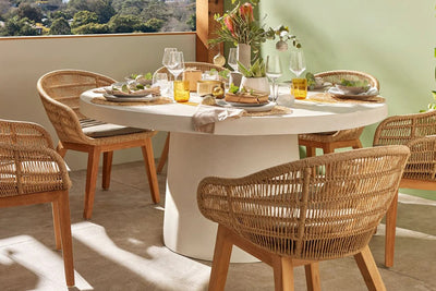 A round concrete outdoor table with five chairs arranged around it, featuring a clean white tabletop, creating a simple dining setup.