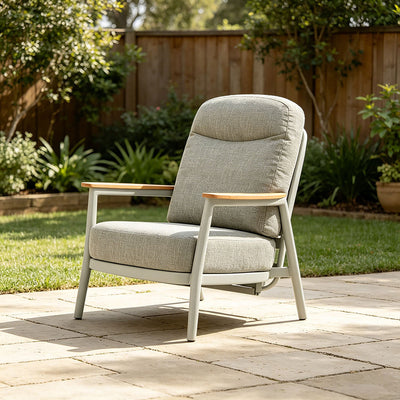 Two sturdy aluminium outdoor armchairs are placed on a wooden deck area overlooking the beach and ocean. Behind one chair, there is a pot plant.