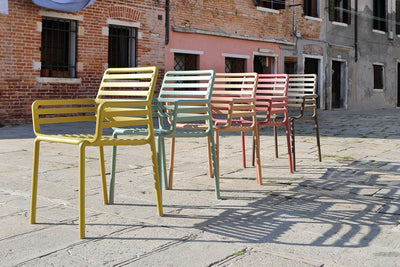 A vibrant display of 5 Nardi chairs in different colours, showcasing the colourful range, set on a stone walkway in a European style street.