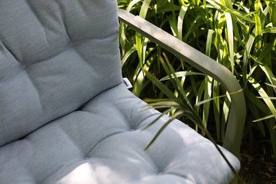 One of our grey Nardi cushions on a green outdoor chair, nestled amongst greenery, offering comfort and style to your outdoor space.