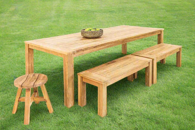 A wooden table accompanied by two matching benches & a stool makes a complete timber outdoor dining set. The furniture is displayed on a field of grass.