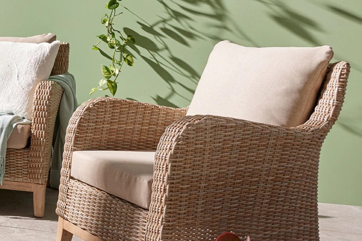 A cozy outdoor wicker armchair beside a vibrant green plant on a sunny patio, creating a serene relaxation space.