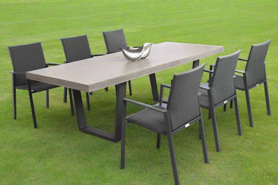 A sturdy outdoor concrete table surrounded by six elegant aluminium outdoor chairs, making a complete concrete outdoor dining set, all set in a sunny grassy field