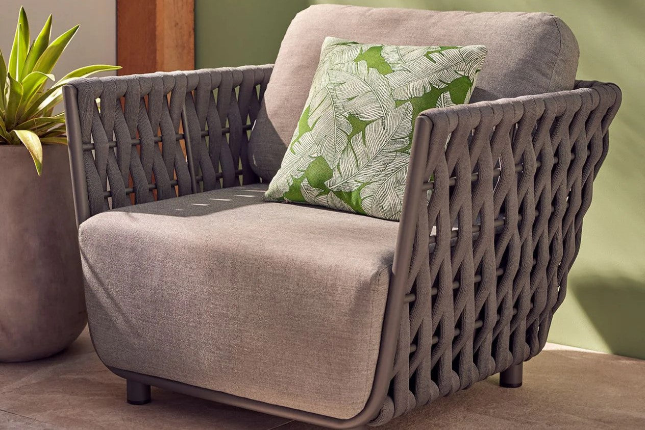 A grey outdoor rope armchair adorned with a green cushion, positioned on a serene patio setting, inviting relaxation and comfort.