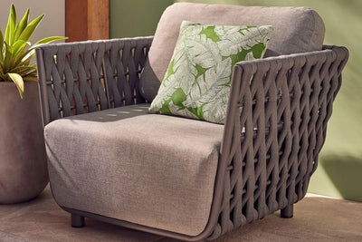 A grey outdoor rope armchair adorned with a green cushion, positioned on a serene patio setting, inviting relaxation and comfort.
