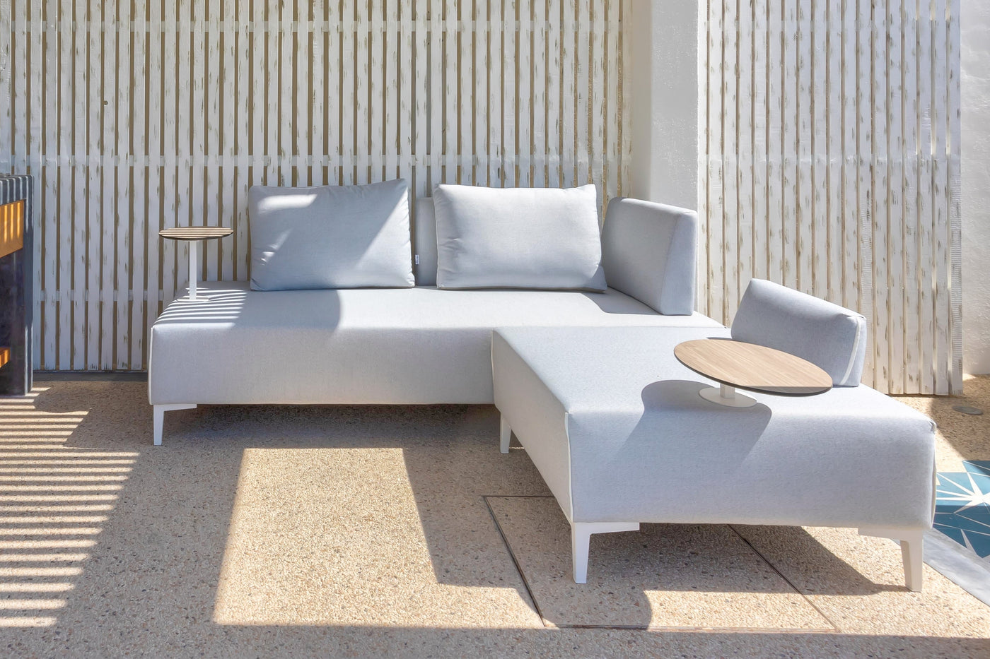 A white luxury outdoor sofa and table basking in the sunlight in a stylish outdoor setting.