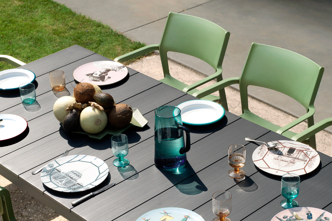 Black Nardi table with cutlery and water, paired with green outdoor chairs, set in a backyard, creating a stylish and functional outdoor dining space.