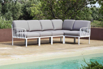 A white & grey resin outdoor modular lounge on a patio, surrounded by lush greenery and a pool.