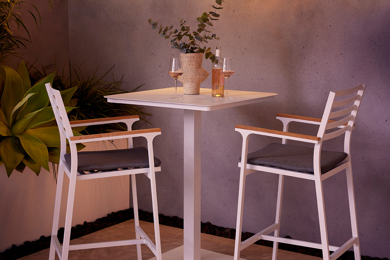 Modern outdoor scene with Spade Wicker Balcony Chair in Black on a white patio, surrounded by greenery, overlooking a serene landscape under a clear blue sky. Sleek Apollo Outdoor Aluminium Round Side Table adds to the contemporary ambiance.