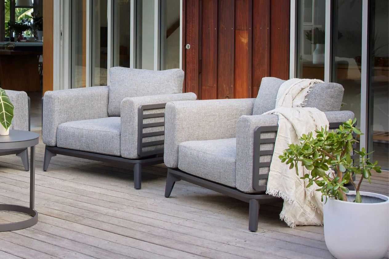 A modern Alora Outdoor Aluminium Armchair in Charcoal with a dark grey frame, light grey cushions, slatted side panels, and tapered legs, displayed against a white background.