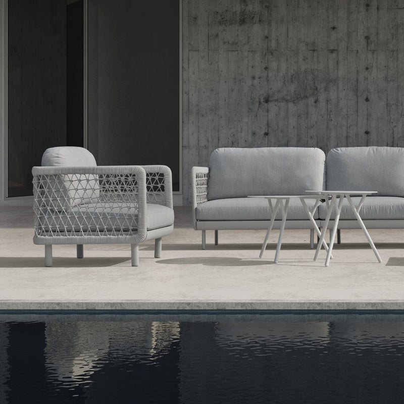 The image displays a modern outdoor armchair featuring a light grey rope design for the armrests and backrest. The seat cushion is a matching light grey, and the chair is set against a neutral outdoor background with stone tiles.