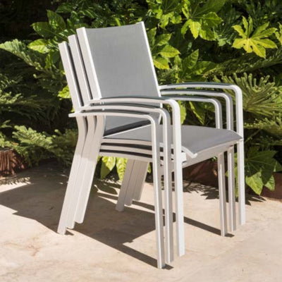 Outdoor furniture: A stack of aluminium dining chairs with teak arms, white frame, and light grey textilene, set against plants.