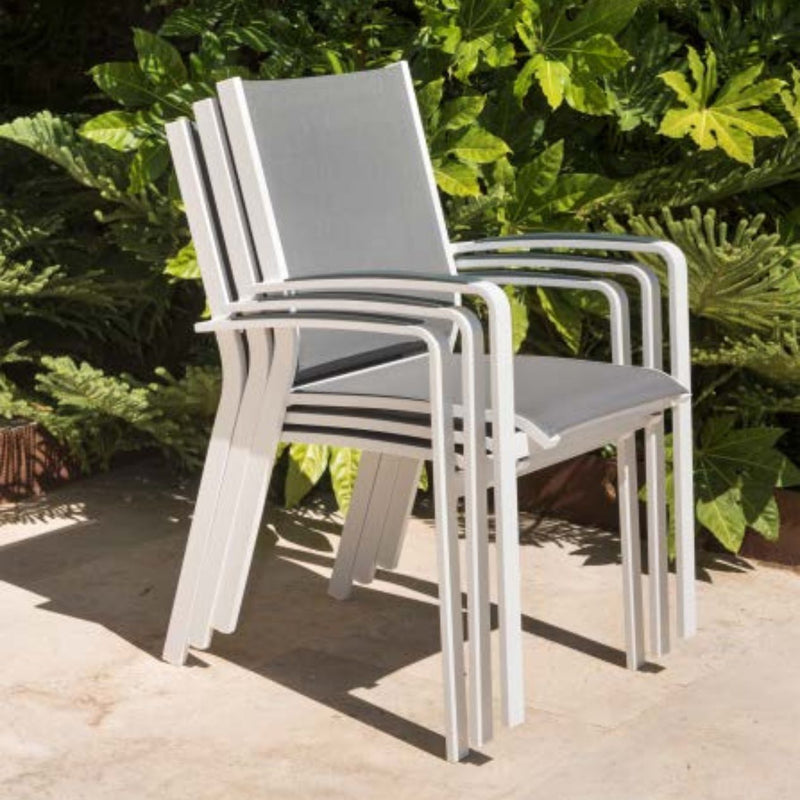 Outdoor furniture: A stack of aluminium dining chairs with teak arms, white frame, and light grey textilene, set against plants.
