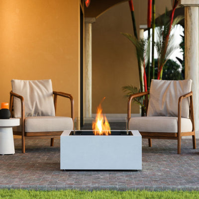 White square EcoSmart Base 30 firepit set in an outdoor area by two outdoor chairs, creating a cozy atmosphere.