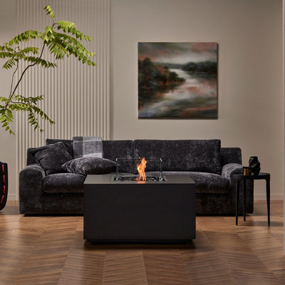 Black square firepit set in a lounge area amongst furniture, creating a cozy and stylish gathering spot.