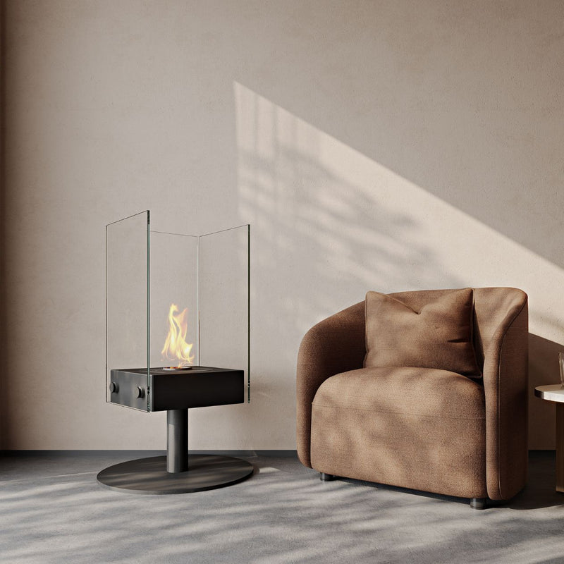 Firepit on a black stand with safety glass surrounding it, set in an indoor area next to a brown armchair, complementing modern furniture arrangements.