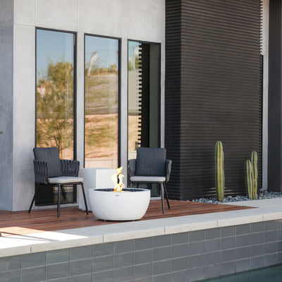 White EcoSmart Pod 30 outdoor firepit set beside 2 chairs outdoors.