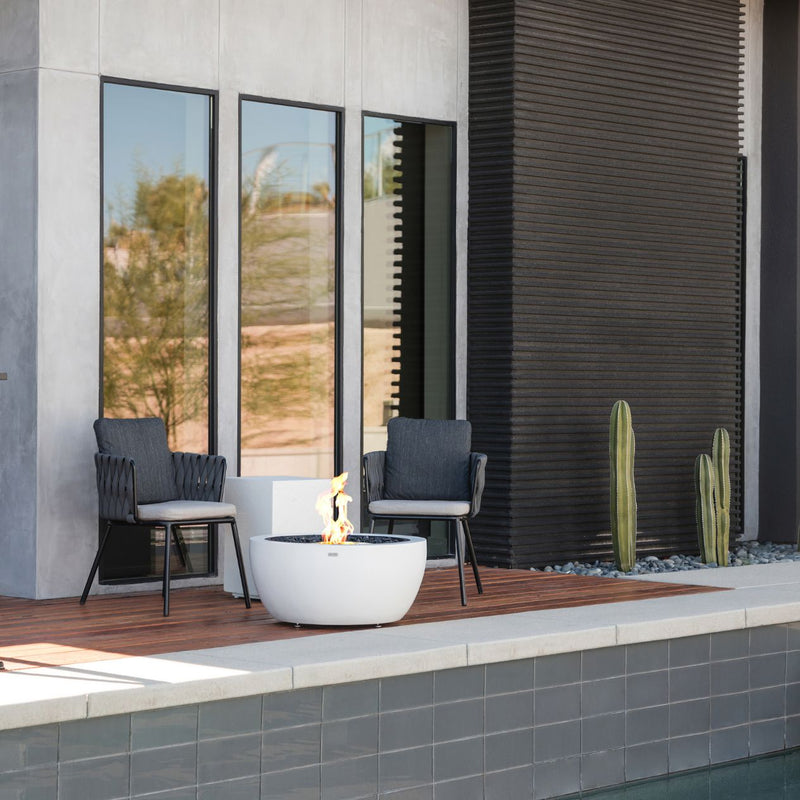White EcoSmart Pod 30 outdoor firepit set beside 2 chairs outdoors.