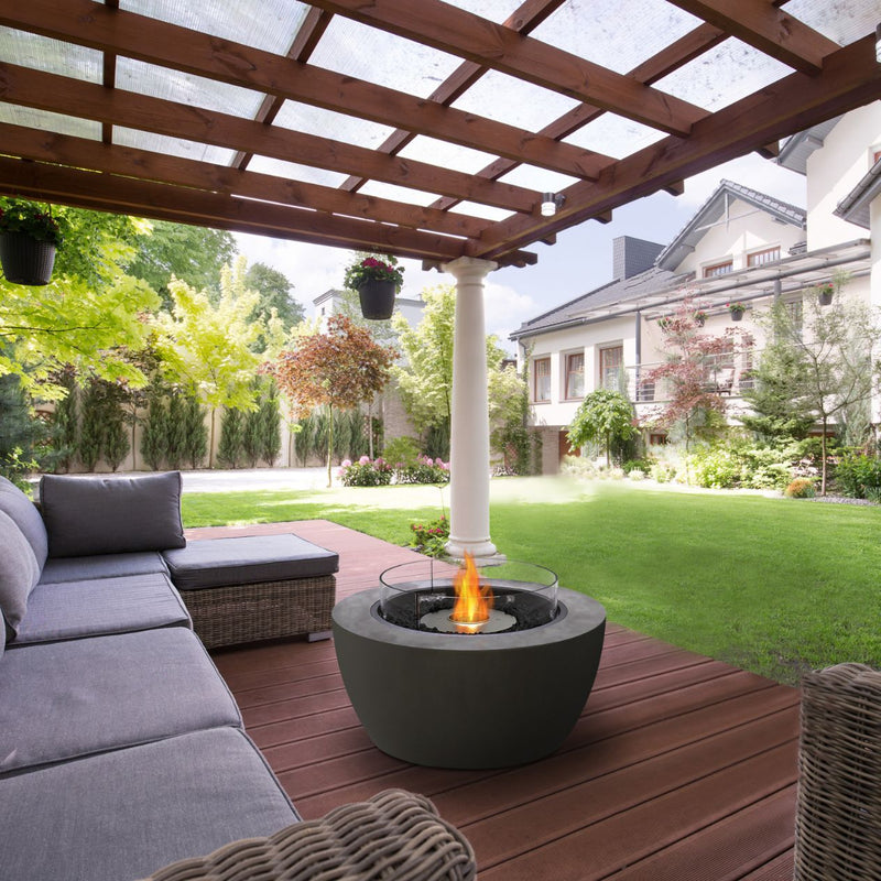 Cylindrical black EcoSmart Pod 40 firepit set in the outdoor patio area of a house alongside an outdoor lounge, creating a warm and inviting space.