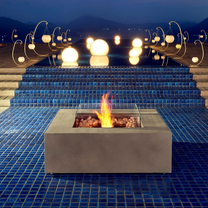 Ecosmart Base 40 square grey firepit placed in an outdoor area by the pool, enhancing the outdoor furniture setting