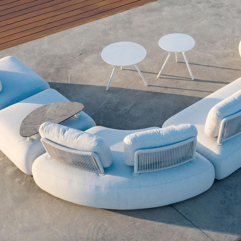 Corner of a light grey Iowa outdoor upholstered modular lounge with two matching aluminium round coffee tables, set on a concrete outdoor area of a modern house, with the sun beaming in, creating a comfortable and inviting outdoor living space.