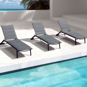 3 sleek black aluminium 'Kent' outdoor sun loungers laying poolside in a luxurious, modern outdoor area of a European-style house, captured from a higher angle, highlighting the symmetry and elegance of the setting.
