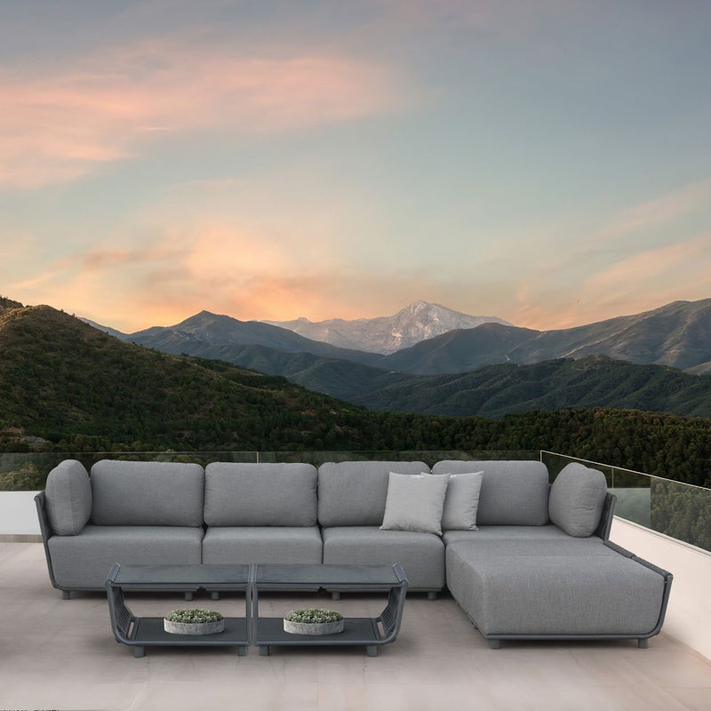 Dark-grey Lawson 7-seater outdoor rope modular lounge with two grey throw pillows, accompanied by two Lawson outdoor coffee tables. The set is placed on a patio, with a stunning sunset backdrop and mountains in the distance, creating a tranquil and stylish outdoor living space.