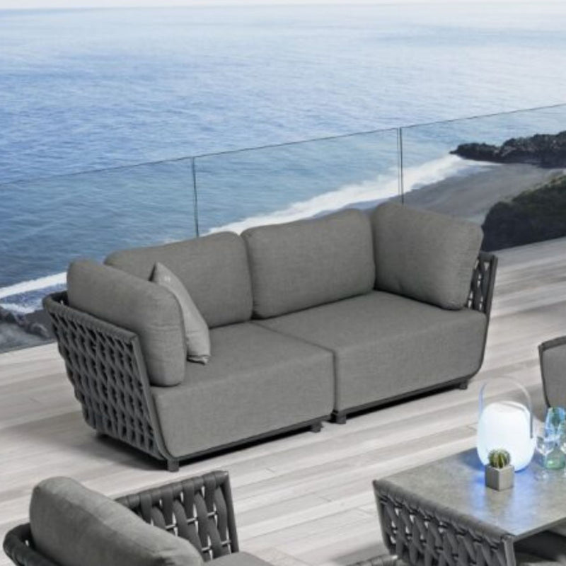 Dark grey two-seater rope lounge set on an outdoor deck of a modern house, overlooking the ocean, perfect for outdoor living.