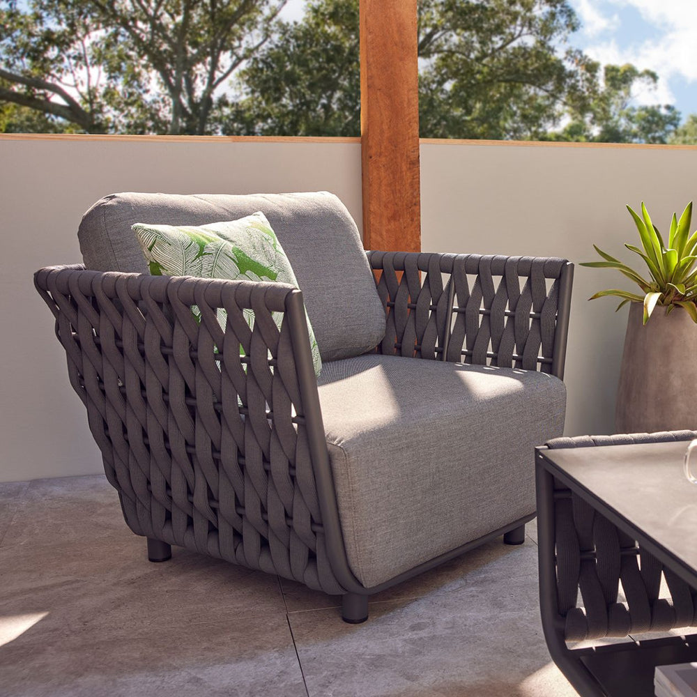 Outdoor furniture set from Lawson Collection featuring a wicker lounge chair, rope armchair with charcoal frame and matching cushions, end chair, ottoman, and coffee table set in a serene backyard.
