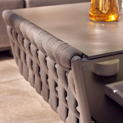 Outdoor furniture from the Lawson Collection, featuring a wicker lounge chair, outdoor dining furniture, and a rope coffee table with a charcoal frame and ceramic glass top, adorned with a small plant and a bowl of starfruit, set in front of a grey sofa.
