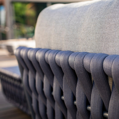 Close-up of a charcoal rope weave on the backrest of an outdoor lounge chair, paired with grey cushions, showcasing intricate craftsmanship and a blend of texture and comfort in a sophisticated outdoor setting.