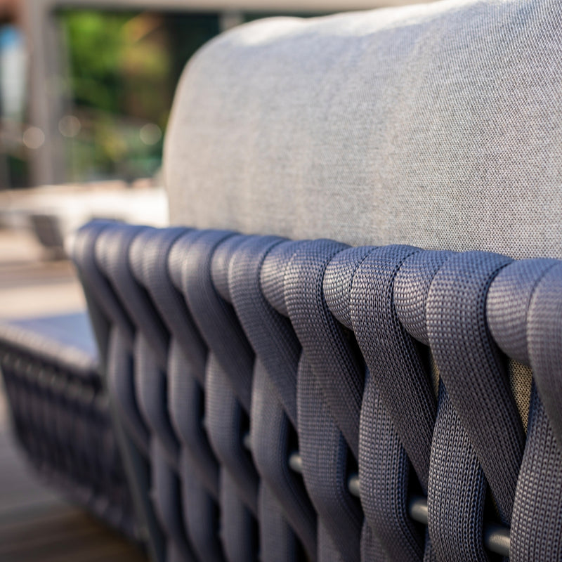 Close-up of a charcoal rope weave on the backrest of an outdoor lounge chair, paired with grey cushions, showcasing intricate craftsmanship and a blend of texture and comfort in a sophisticated outdoor setting.