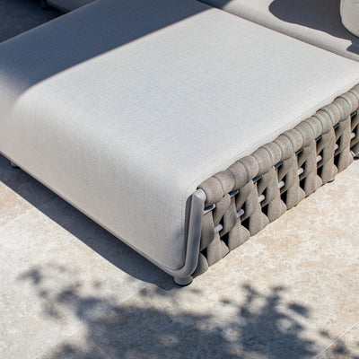 Close-up of a taupe outdoor lounge with light sand-coloured cushions and intricately woven rope detailing along the base, highlighting its elegant design and craftsmanship on a sunlit tiled patio.