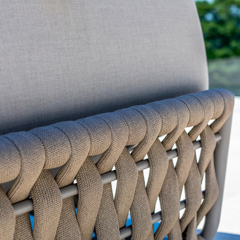 Close-up of the taupe rope detailing and light sand-coloured cushions of an outdoor sun lounger, highlighting the woven craftsmanship and premium fabric against a serene outdoor backdrop.