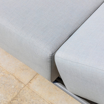 Close-up of the clean, seamless edges and soft grey upholstery of a modular outdoor sun lounger, highlighting its refined craftsmanship and durable fabric, set on a textured tiled patio.
