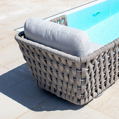 Close-up view of a Taupe rope swivel chair with woven detailing, featuring soft light sand grey cushions, positioned on a tiled patio beside a sparkling blue pool, highlighting the craftsmanship and elegance of outdoor furniture in a sunny setting.