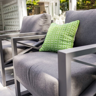 Aluminum outdoor furniture from Linear Lounge collection, including outdoor chairs and outdoor lounge, in charcoal or white. A grey couch with a green pillow on it.