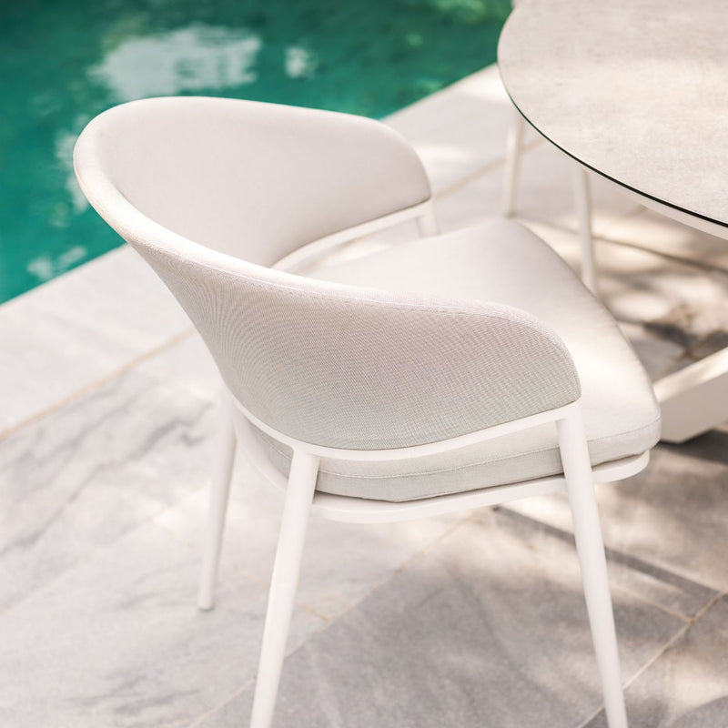 A white aluminum Medea outdoor dining chair with sleek zip-off cushion covers, placed by an outdoor dining table in a backyard by a pool.