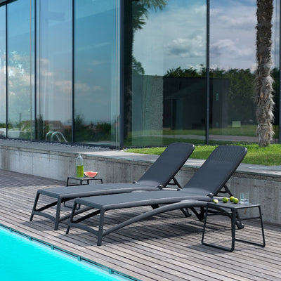Two black resin 'Nardi' sun loungers with textilene seat and backrest, each paired with a matching black outdoor coffee table, set poolside with a super modern house in the background.