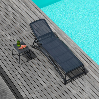 Black resin 'Nardi' sun lounger with textilene seat and backrest, accompanied by a matching black outdoor coffee table, set poolside on a wooden deck with the sun shining in.