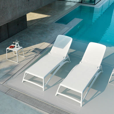 Two white resin 'Nardi' sun loungers with textilene seats and backrests, set poolside with a matching coffee table on one side. All the furniture is set against the backdrop of a super modern brutalist Italian-style outdoor area of a house.