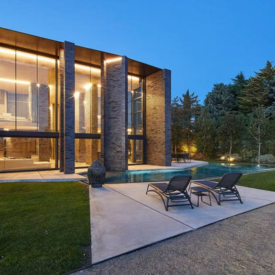 Two black resin 'Nardi' sun loungers with textilene seat and backrest, positioned poolside with one coffee table in between, all facing a super modern house in the outdoor area.
